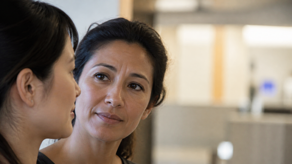 Two women healthcare professionals in conversation at a softly lit nurses' station