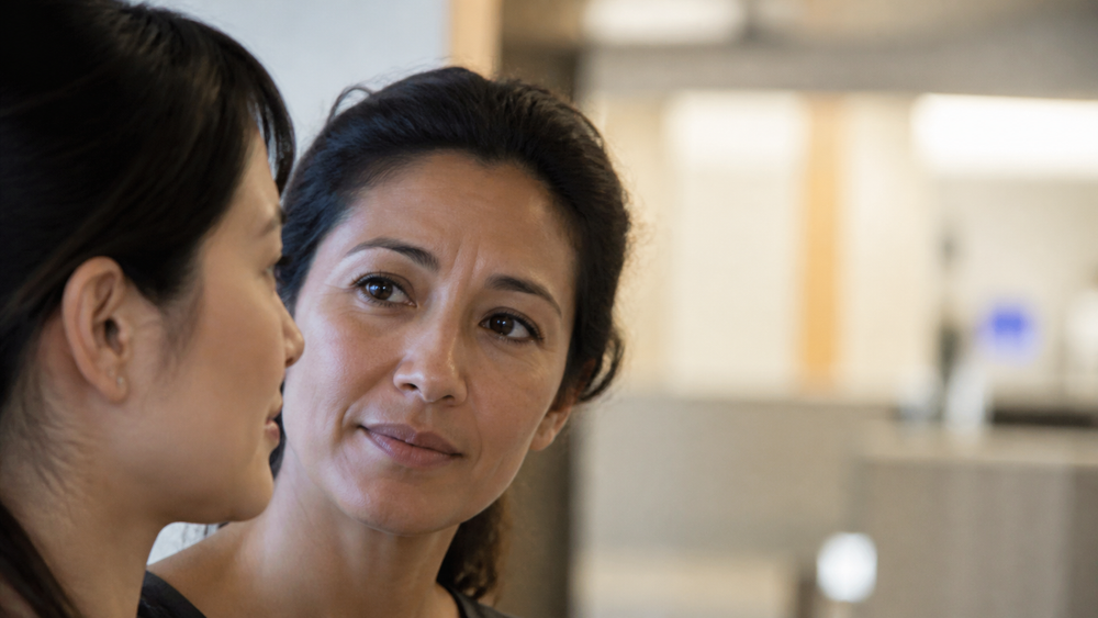 Two women healthcare professionals in conversation at a softly lit nurses' station